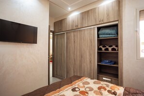 Ein Schlafzimmer mit Kleiderschrank, Bett und einem an der Wand befestigten Fernseher.