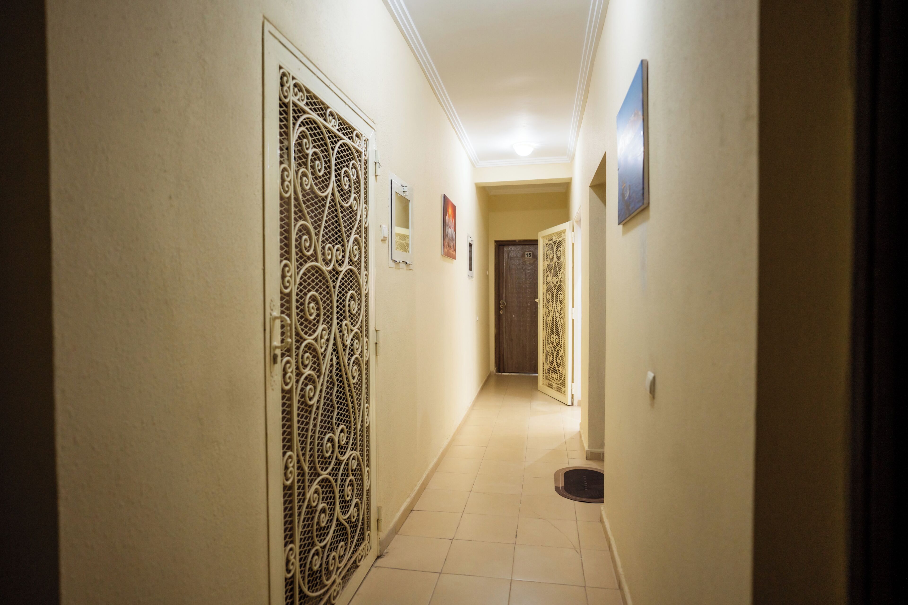 Um corredor com um portão de metal decorativo, uma porta com número e um quadro na parede.