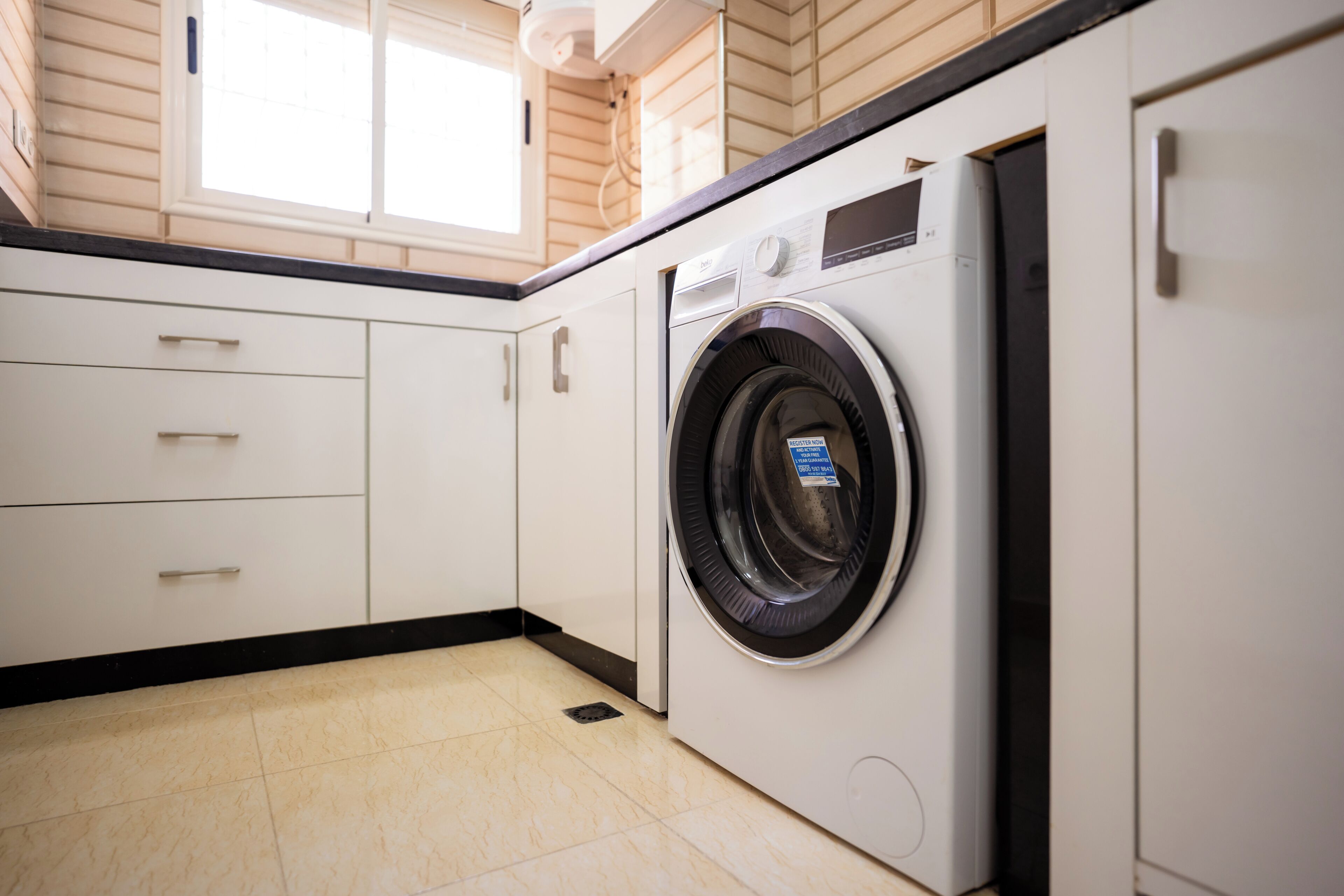 A compact laundry room with a front-loading washing machine, white cabinets, and a window providing natural light.