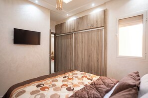 A bedroom with a bed, a wardrobe, a television, and a window. - Authentic Moroccan Apt 2BR 8 min Airport AC and Parking Marrakech (Marrakech)