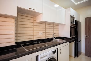 A compact kitchen with a black countertop, stainless steel appliances, and a built-in washing machine.
