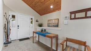A hallway with a wooden ceiling, a white door, a bench, a table with a blue cloth, and a framed picture on the wall. - Four Bedroom Home with War Eagle River View and Access (Rogers)
