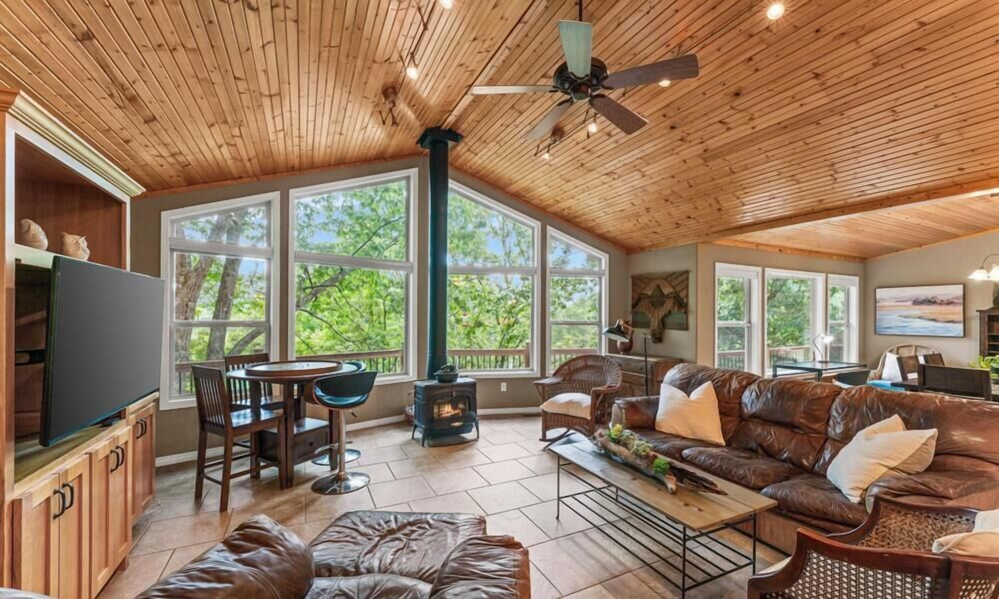 Amplia sala de estar con chimenea, mobiliario de cuero y ventanas grandes que ofrecen vistas al exterior.