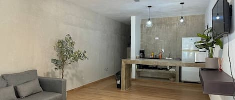 A living room with a sofa, a dining table, a ceiling fan, a TV, and a plant.