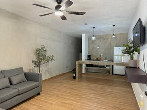 Un salon comprenant un canapé, une table à manger, un ventilateur de plafond, un téléviseur et une plante.