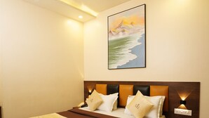A hotel room with a large bed, a ceiling fan, a painting on the wall, and a nightstand with a lamp. - Hotel Royace Executive By Glitz Hotels (Mumbai)