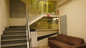 A staircase with a handrail leading to a landing area with a brown sofa and a small table. - Hotel Royace Executive By Glitz Hotels (Mumbai)