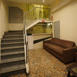 A staircase with a handrail leading to a landing area with a brown sofa and a small table. - Hotel Royace Executive By Glitz Hotels (Mumbai)