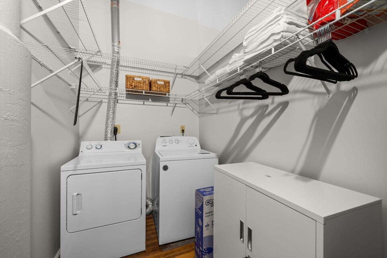 A laundry room with two washing machines, a drying rack, and a storage cabinet.