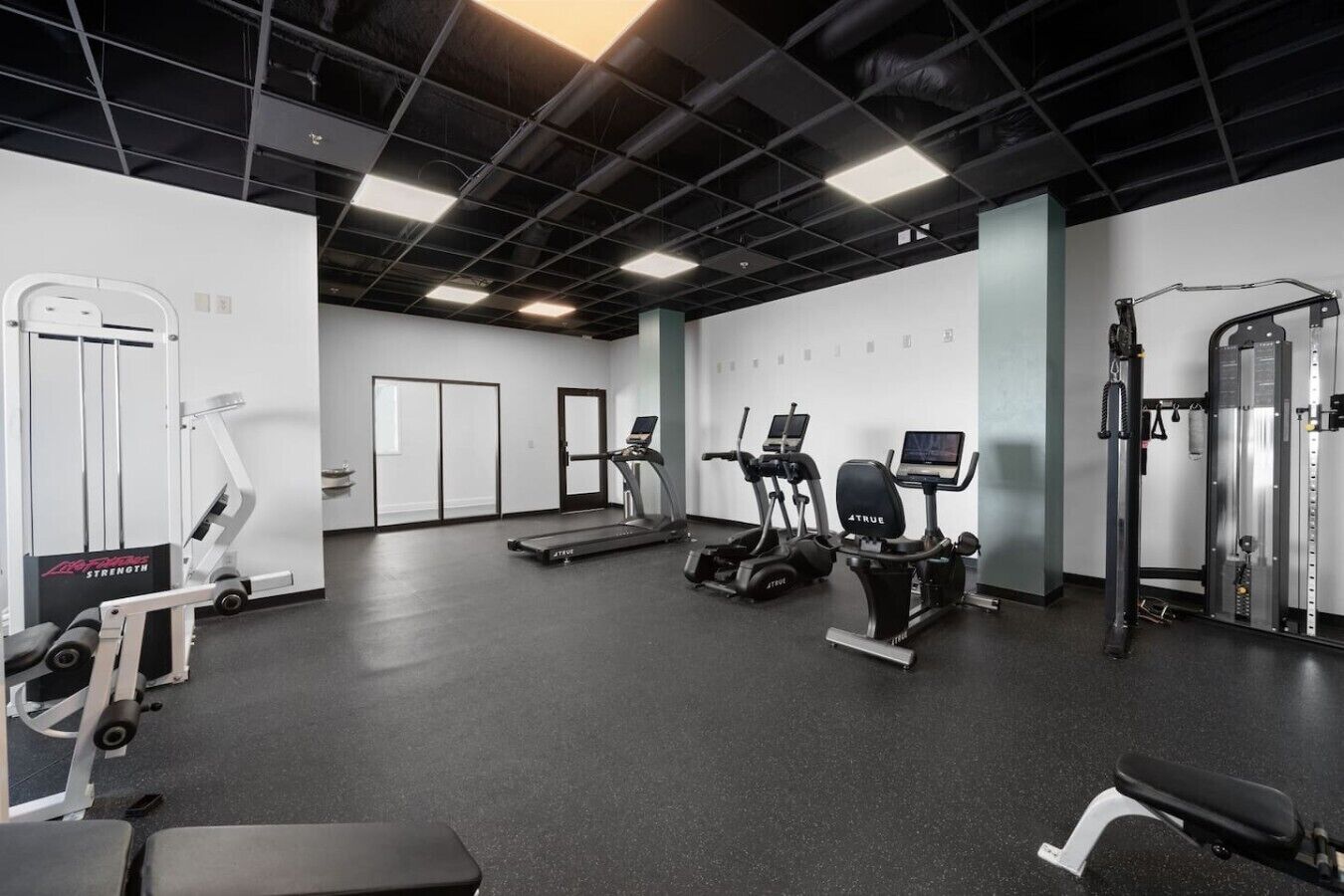 A gym with cardio machines, weightlifting equipment, and a mirrored wall.