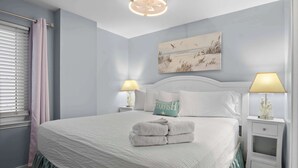Een net opgemaakt bed met een witte dekbedovertrek en een groene hoeslaken, twee nachtlampjes, een nachtkastje met een decoratief object, en een schilderij boven het bed.