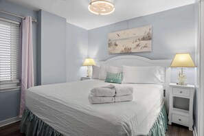 Ein ordentlich bezogenes Bett mit weißer Decke und grünem Bettschlitten, zwei Nachttischlampen, ein Nachttisch mit einer Dekoration und ein Gemälde über dem Bett.