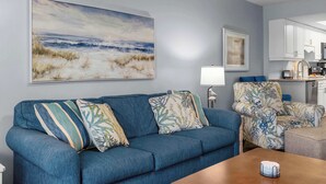 Een woonkamer met een blauwe bank, een bijzettafeltje en een schilderij van een strandgezicht.