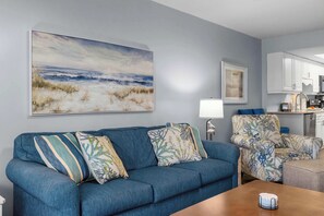 Ein Wohnzimmer mit einem blauen Sofa, einem Couchtisch und einem Gemälde mit Strandmotiv.