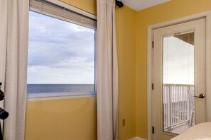 Ein Zimmer mit Meerblick durch ein Fenster, eine Tür mit Moskitonetz und eine gelbe Wand.