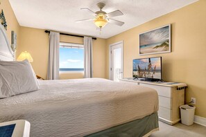 Ein Schlafzimmer mit einem Bett, einem Deckenventilator, einem Fenster mit Vorhängen, einem Fernseher und Kunstwerken an der Wand.