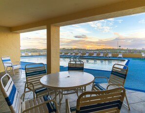 Ein überdachter Außenbereich mit Pool und Liegestühlen, der auf ein Gewässer und einen Sonnenuntergang Blick bietet.