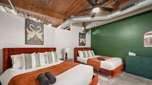 Une chambre d’hôtel avec deux lits, un mur d’accent vert, un ventilateur de plafond et une commode verte.