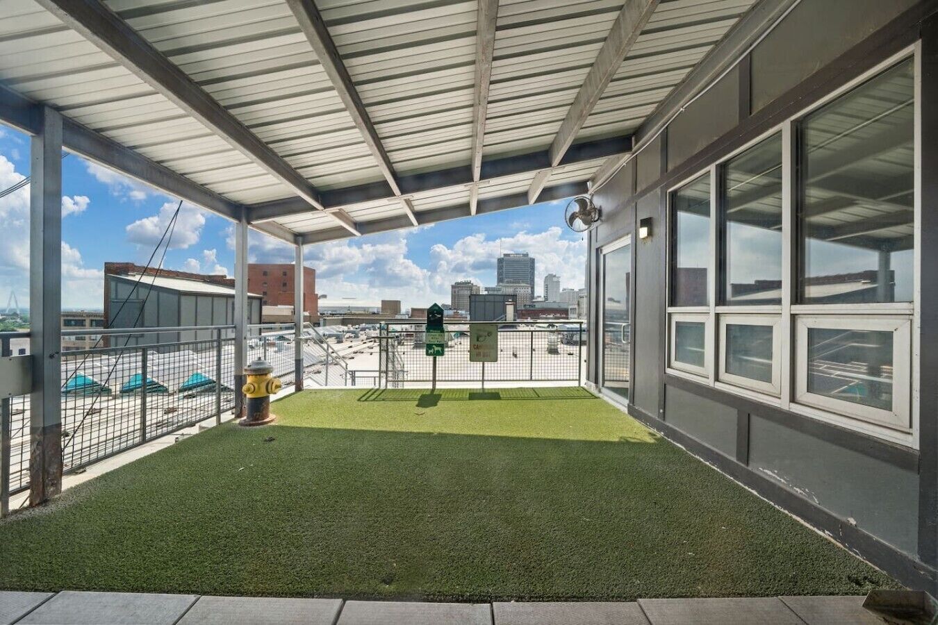A covered outdoor area with artificial grass, a fenced-in space, and a view of the city skyline.