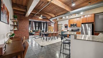 A modern kitchen with stainless steel appliances, a dining area with a wooden table and chairs, and a brick wall.