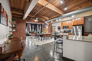 Une cuisine moderne dotée d’appareils électroménagers en acier inoxydable, un coin repas avec une table et des chaises en bois, et un mur en briques.