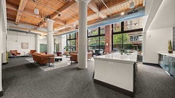 An open-plan office space with high ceilings, exposed ductwork, and large windows offering views of the outside.