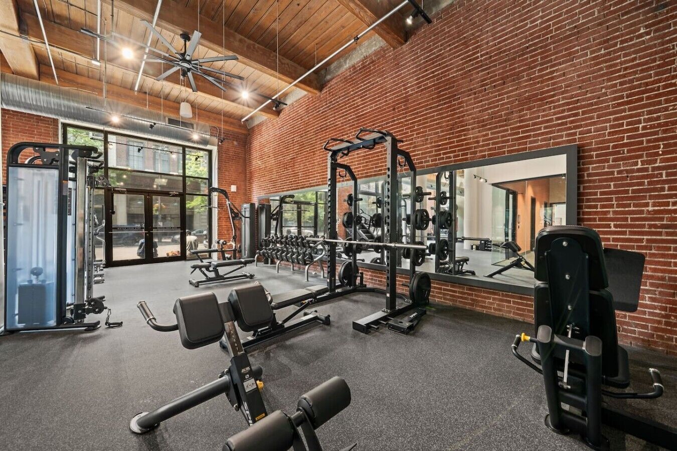A gym with various exercise equipment, a large mirror, and a brick wall.