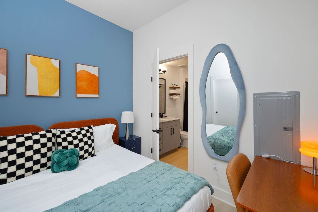 Una habitación de hotel con cama, escritorio, silla, baño y espejo.