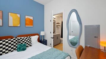 Una habitación de hotel con cama, escritorio, silla, baño y espejo.
