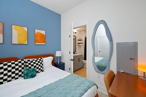 A hotel room with a bed, a desk, a chair, a bathroom, and a mirror.