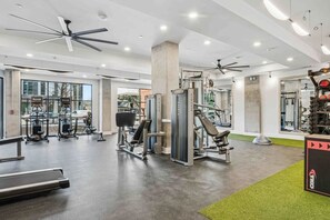 A modern gym with ceiling fans, various exercise equipment, and a large mirror. - Loft  w/ King Bed, Balcony, Gym, Courtyard w/ Grilling Station & Free Parking (Charlotte)