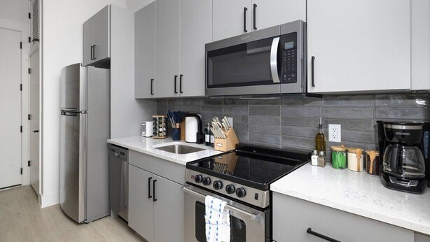 Uma cozinha moderna com eletrodomésticos de aço inoxidável, incluindo geladeira, micro-ondas, fogão e lava-louças.