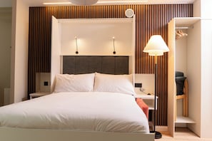 Una habitación de hotel moderna con una cama, mesitas de noche, un escritorio y un armario.