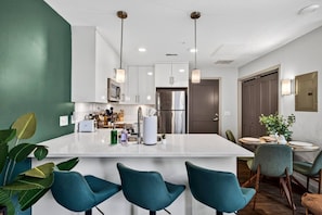 Uma cozinha moderna com uma ilha central, banquetas de bar e uma área de refeições com mesa e cadeiras.