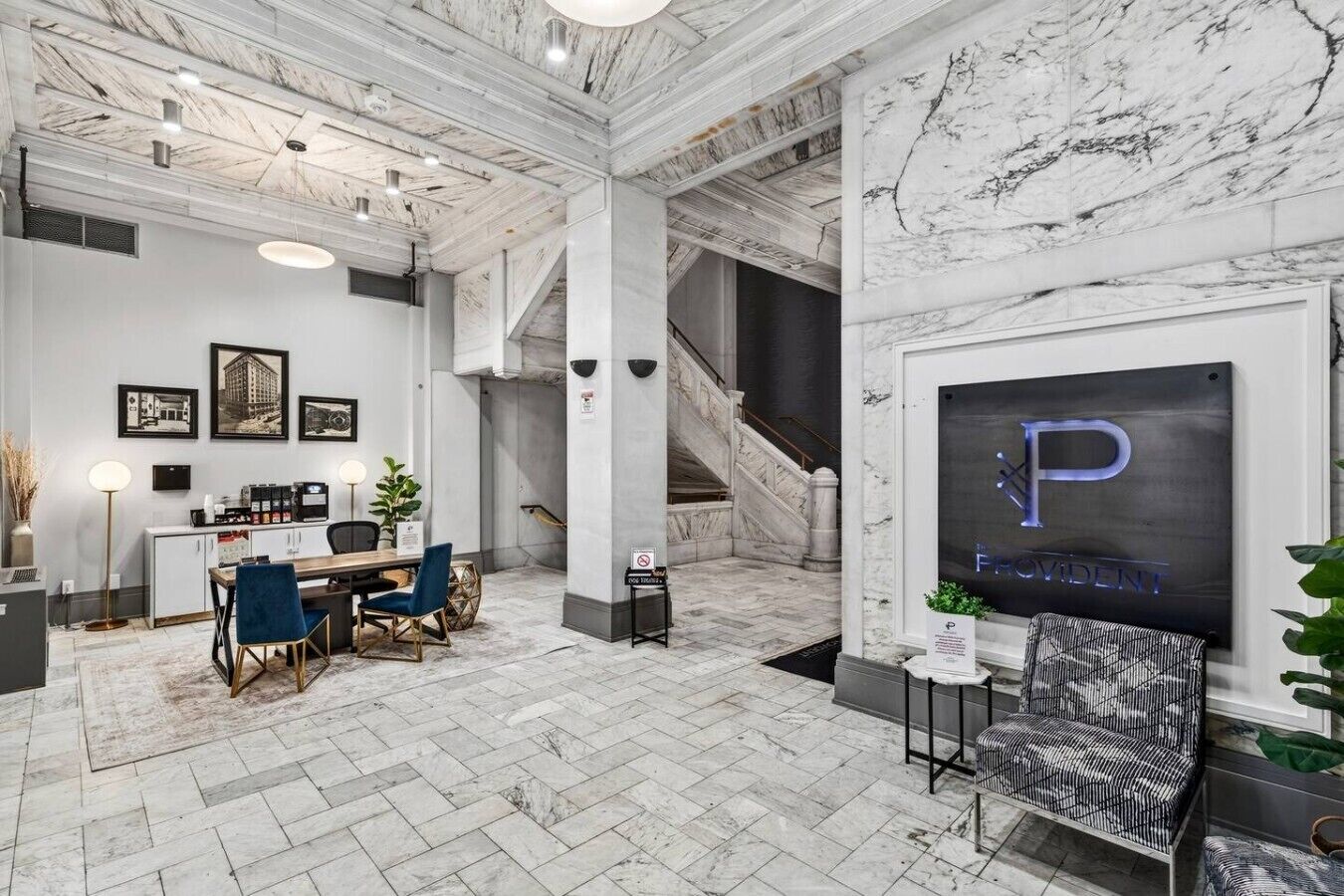 A spacious lobby with a marble floor, a reception desk, a staircase, and a framed sign with the letter 'P'.