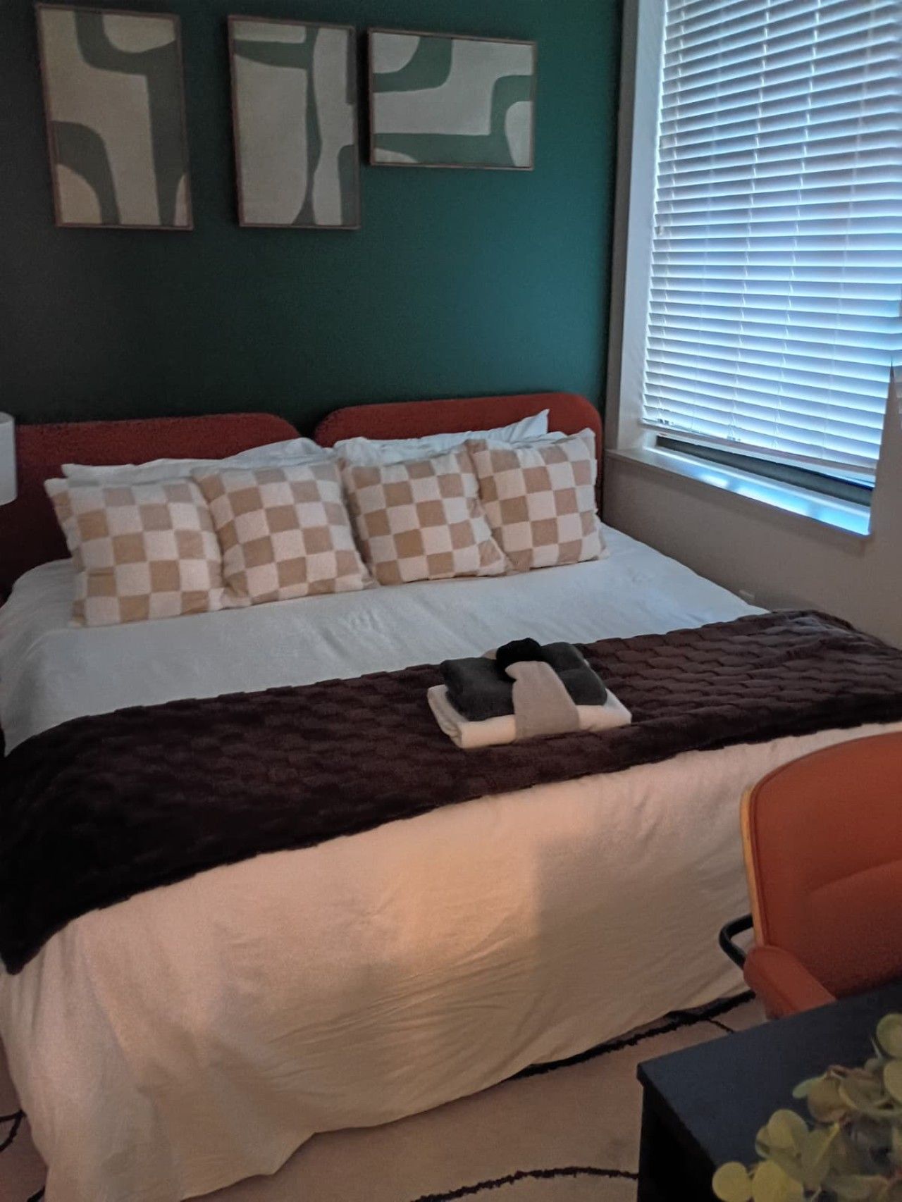 Quarto com cama, almofadas, cobertor, uma cadeira e obras de arte na parede.