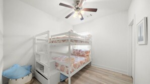 A bunk bed room with a ceiling fan, a small storage basket, and a framed picture on the wall. - Cozy Family Home, Prime Location Near Downtown (Galveston)