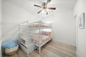 Quarto com beliche, ventoinha no teto, cesto de armazenamento pequeno e quadro na parede.