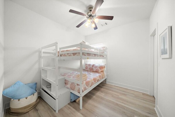 Een slaapkamer met stapelbed, plafondventilator, klein opbergmandje en een ingelijste foto aan de muur.
