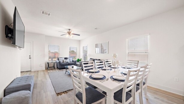 A modern living room with a dining area, a flat-screen TV mounted on the wall, and a ceiling fan. - Cozy Family Home, Prime Location Near Downtown (Galveston)