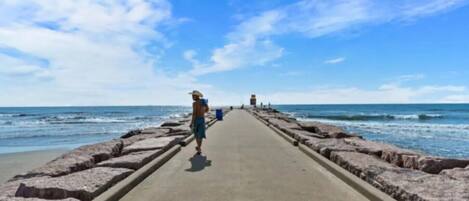 Un sendero de concreto que lleva a la playa, con una persona alejándose de la cámara.