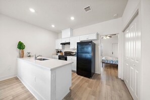 A modern kitchen with white cabinetry, a black refrigerator, and a wooden floor. - Cozy Family Home, Prime Location Near Downtown (Galveston)