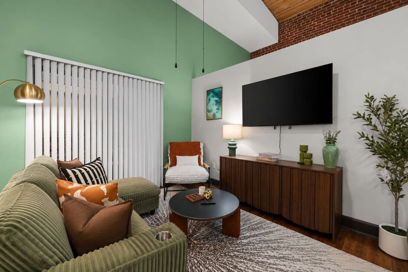 Ein Wohnzimmer mit Sofa, Sessel, Couchtisch und an der Wand montiertem Fernseher.