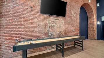A room with a brick wall, a flat-screen TV mounted above a shuffleboard table.