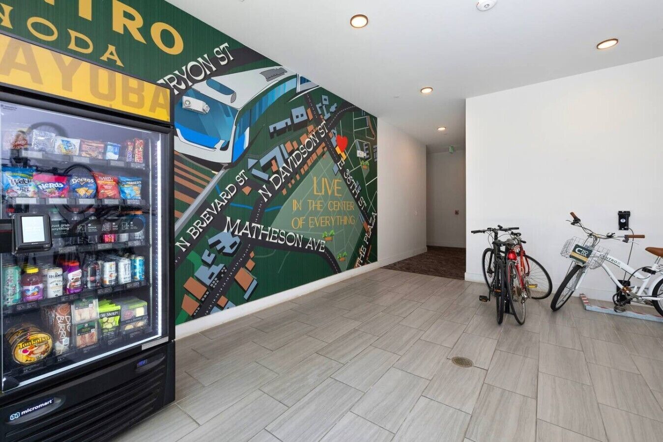 Máquina expendedora llena de bocadillos y un mural que muestra un paisaje urbano con una bicicleta.