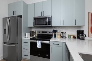 Una cocina moderna con electrodomésticos de acero inoxidable, armarios de color gris claro y una encimera blanca.