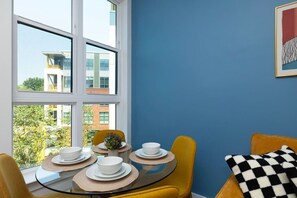 Comedor con una mesa dispuesta para cuatro, sillas amarillas y vista a edificios a través de amplios ventanales.
