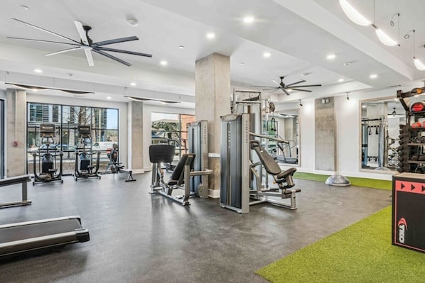 A modern gym with ceiling fans, various exercise equipment, and a large mirror.