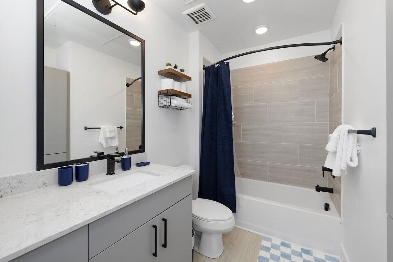 Un bagno moderno con un water bianco, un lavabo con piano in marmo, uno specchio grande e una zona doccia con soffione curvo.