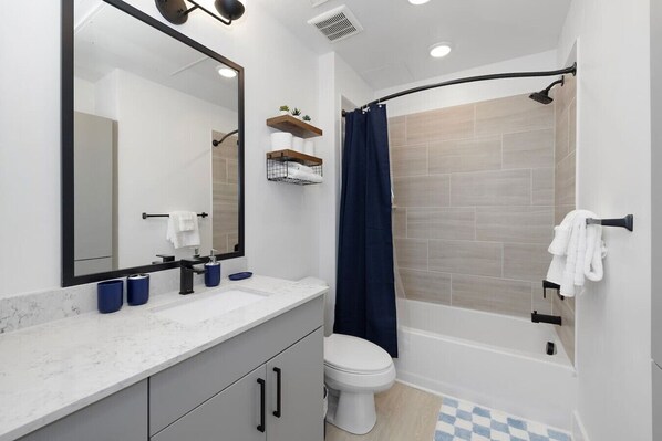 A modern bathroom with a white toilet, a sink with a marble countertop, a large mirror, and a shower area with a curved showerhead.